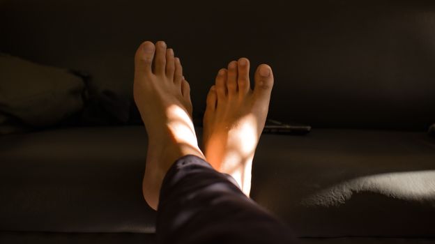 A close-up view of relaxed barefoot on a couch with soft lighting creating a serene mood.