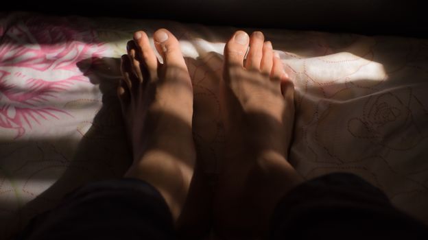 A close-up shot of bare feet casting shadows on a patterned bedspread.