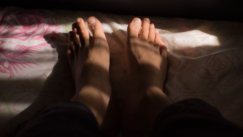 A close-up shot of bare feet casting shadows on a patterned bedspread.