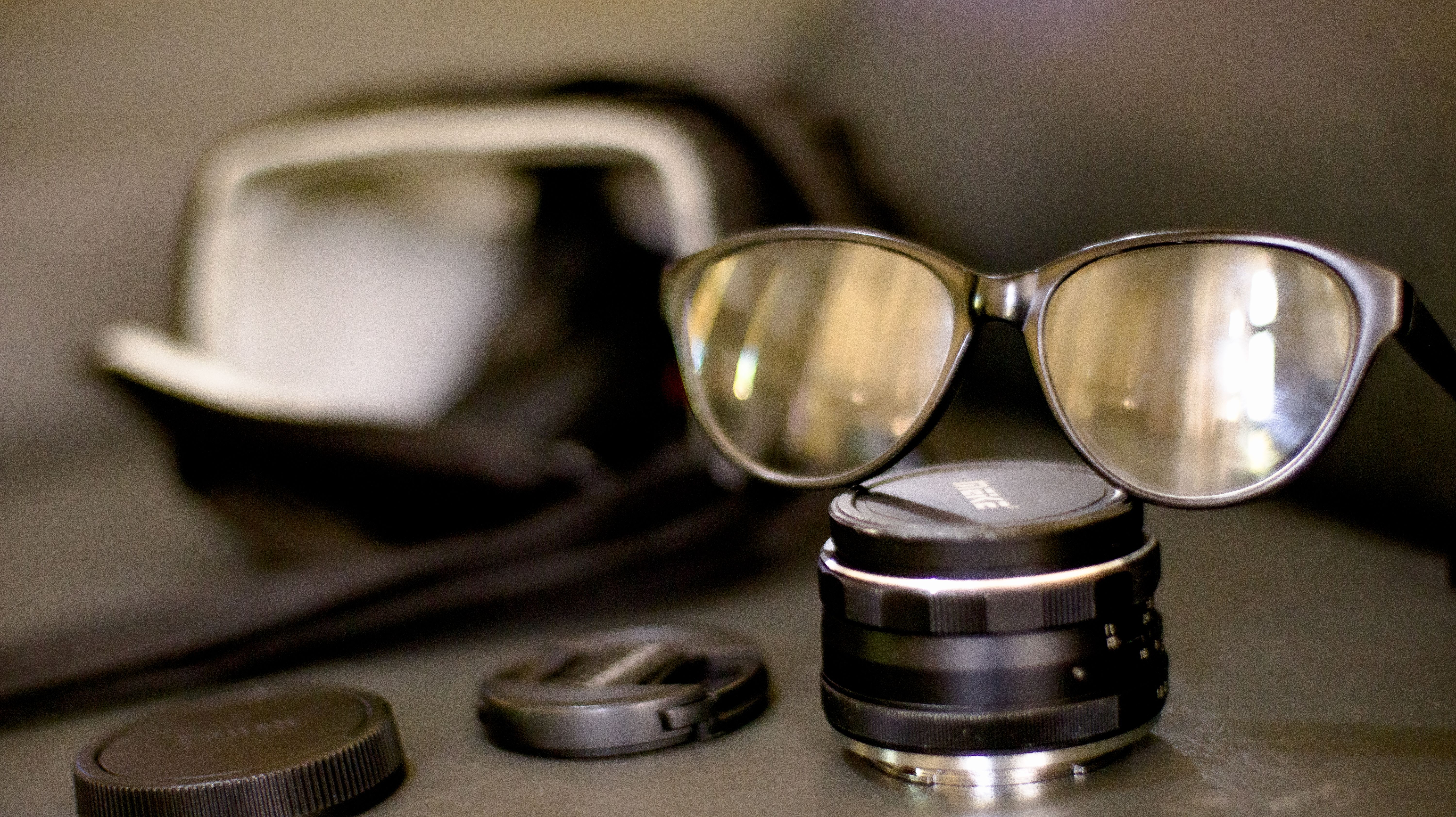 Closeup glasses in black rim on black photography lens placed on black table in front of photo bag