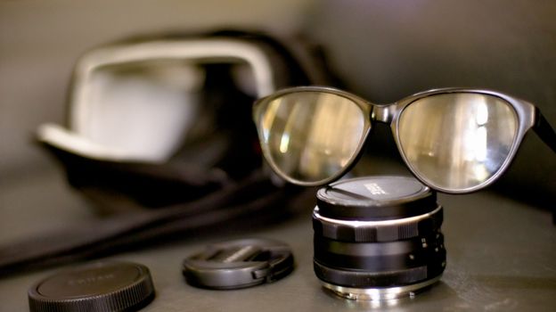 Closeup glasses in black rim on black photography lens placed on black table in front of photo bag