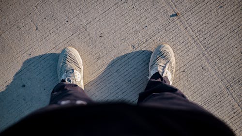 Top view of crop anonymous person in sneakers and activewear standing on road after outdoor training in sunny morning