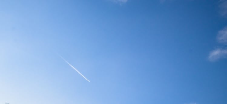 A Jet Flying Under Blue Sky Leaving A Line Of White Smoke 
 