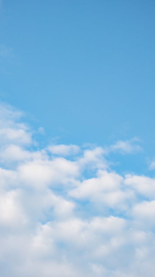 From below of small white fluffy clouds floating in blue sky in daylight