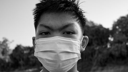 Free Black and white young ethnic male wearing medical mask and looking at camera with lush greenery on background Stock Photo