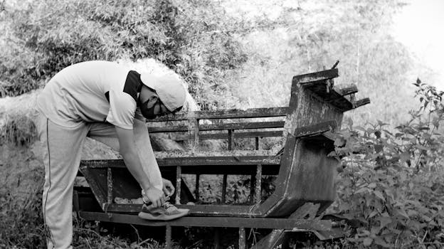 A man ties his shoelaces during a quiet outdoor moment by an old bench, wearing activewear and a cap.