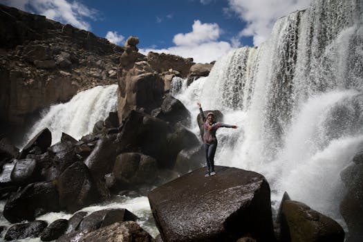 A woman posing confidently on rocks near a powerful waterfall in Peru's rugged landscape.