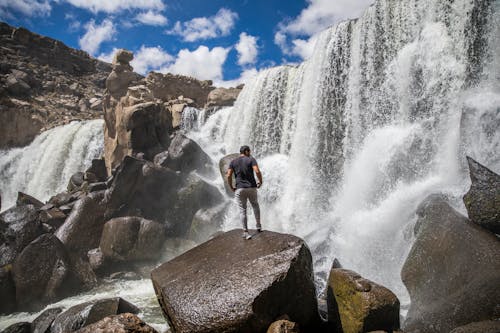 Free Man standing on a Boulder near Waterfalls  Stock Photo