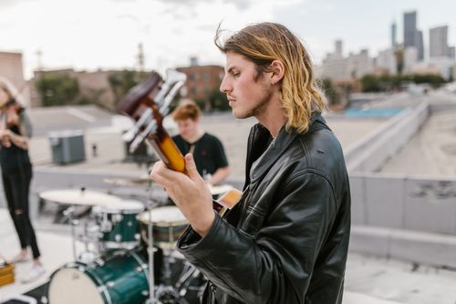 Free Guitarist in black leather jacket plays on rooftop with city backdrop. Stock Photo