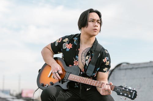 A Man in Black Floral Button Up Shirt Playing Guitar