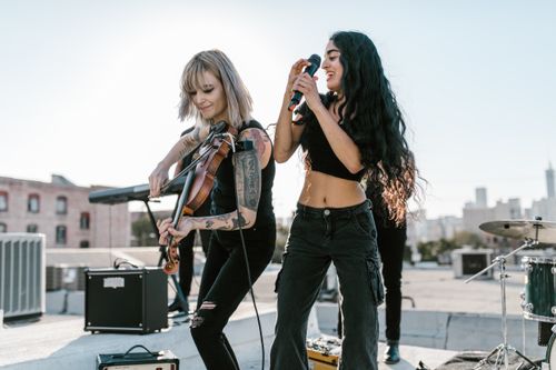 Free Two female musicians performing on a rooftop with violin and microphone, enjoying an energetic music session. Stock Photo