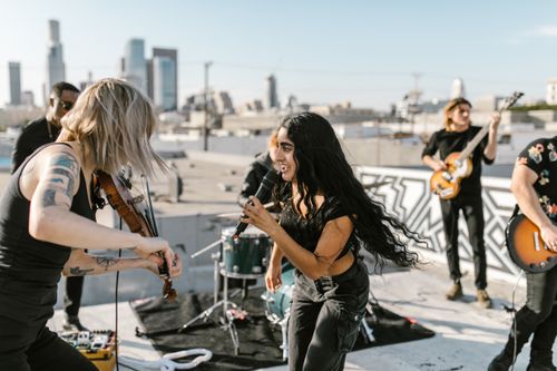 Free Indie band performing a lively rooftop concert with skyline in the background. Stock Photo