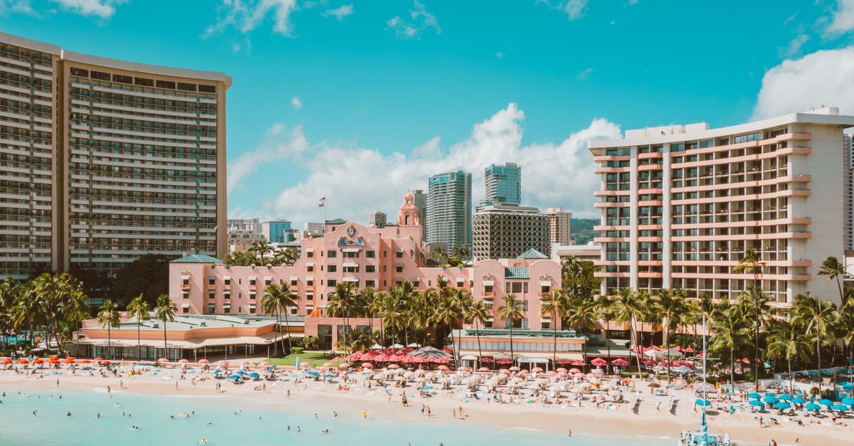 Photo by Jess Loiterton A stunning view of Waikiki Beach with vibrant city skyscrapers and lush palm trees.