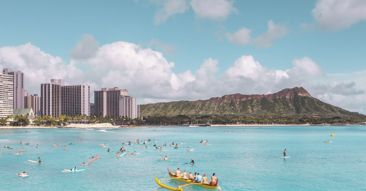 Photo by Jess Loiterton Vibrant summer scene at Waikiki Beach with people kayaking and surfing, set against Diamond Head.