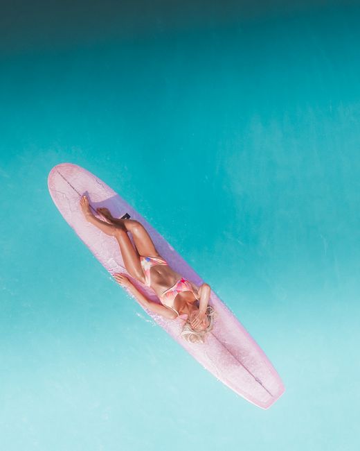 Aerial shot of a woman in a bikini lounging on a surfboard over vibrant turquoise waters.