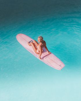 A woman sits on a pink surfboard enjoying the clear turquoise waters of the ocean.