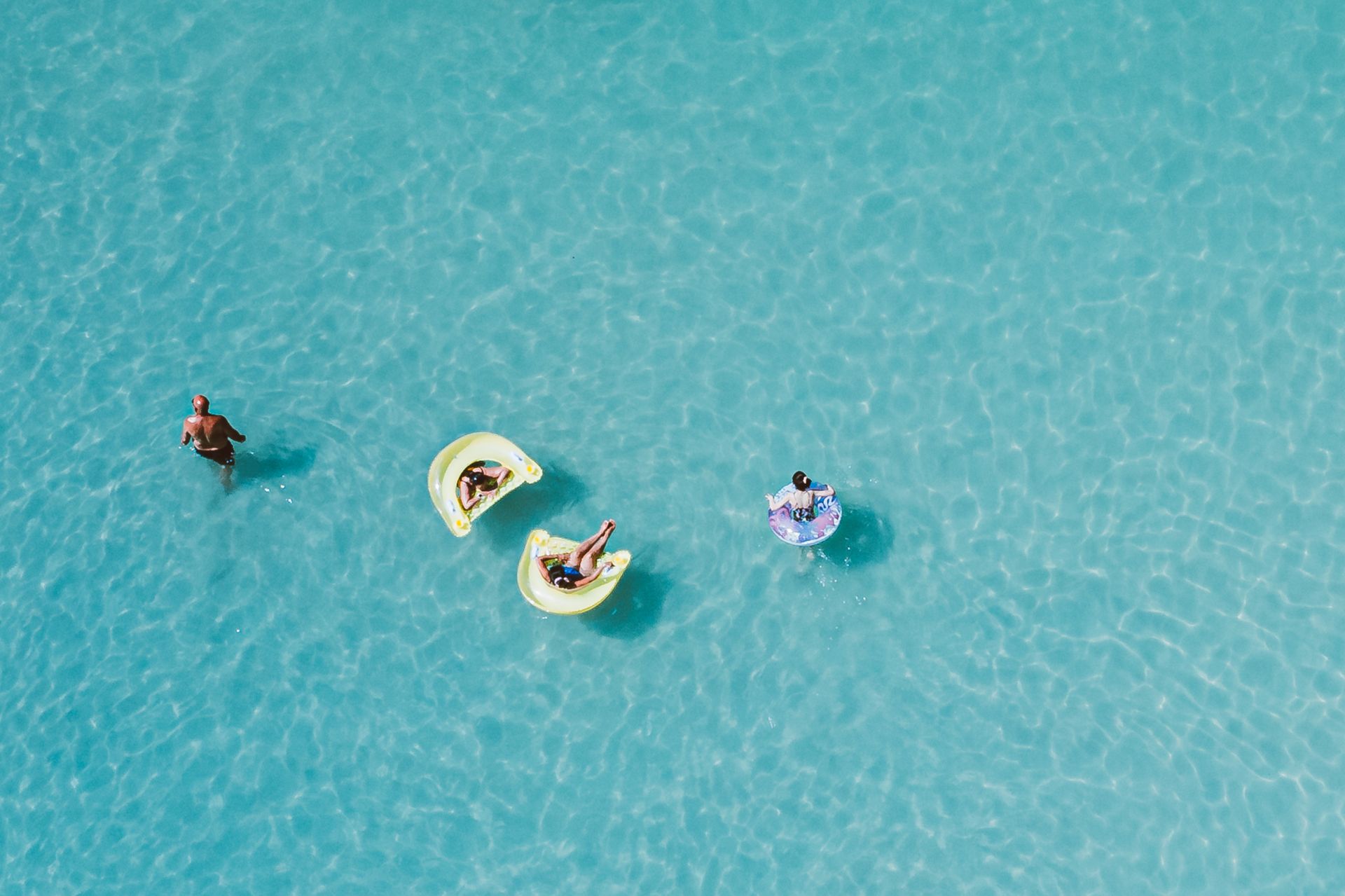 Aerial shot of people relaxing on float tubes in beautiful blue water, enjoying leisure time.