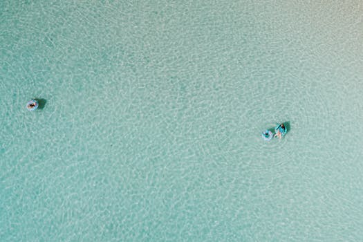 Drone shot capturing people leisurely floating on clear turquoise water with float tubes.