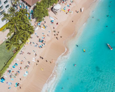 Aerial view capturing people enjoying a sunny day at the beach with turquoise waters and vibrant surroundings.