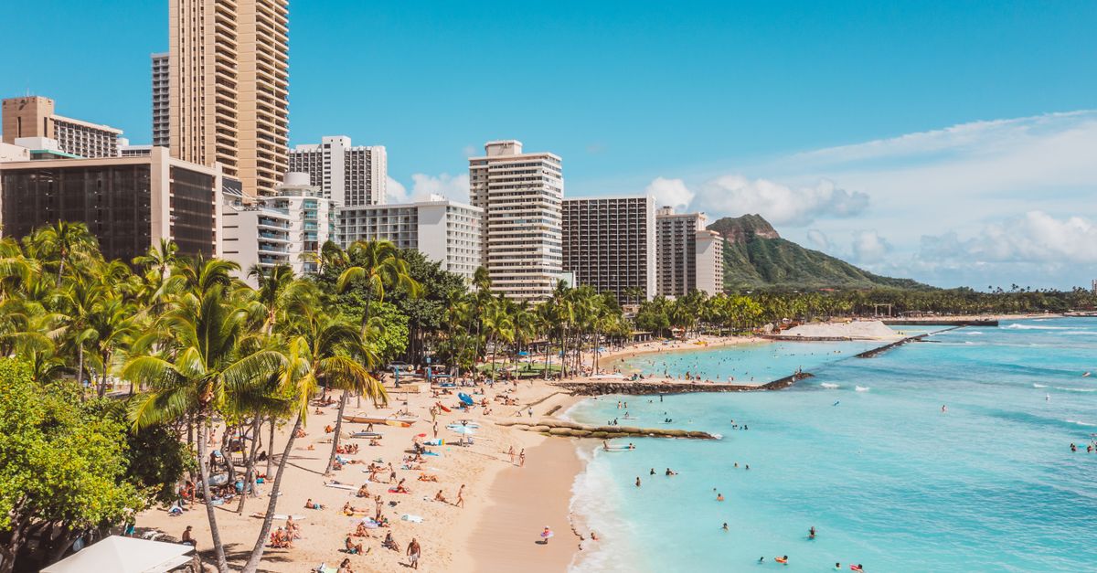 Photo by Jess Loiterton A bustling Waikiki Beach scene with skyscrapers and Diamond Head in the background, highlighting a popular travel destination.