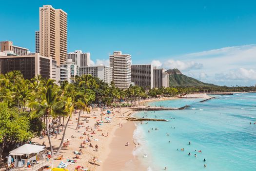 Photo by Jess Loiterton A bustling Waikiki Beach scene with skyscrapers and Diamond Head in the background, highlighting a popular travel destination.