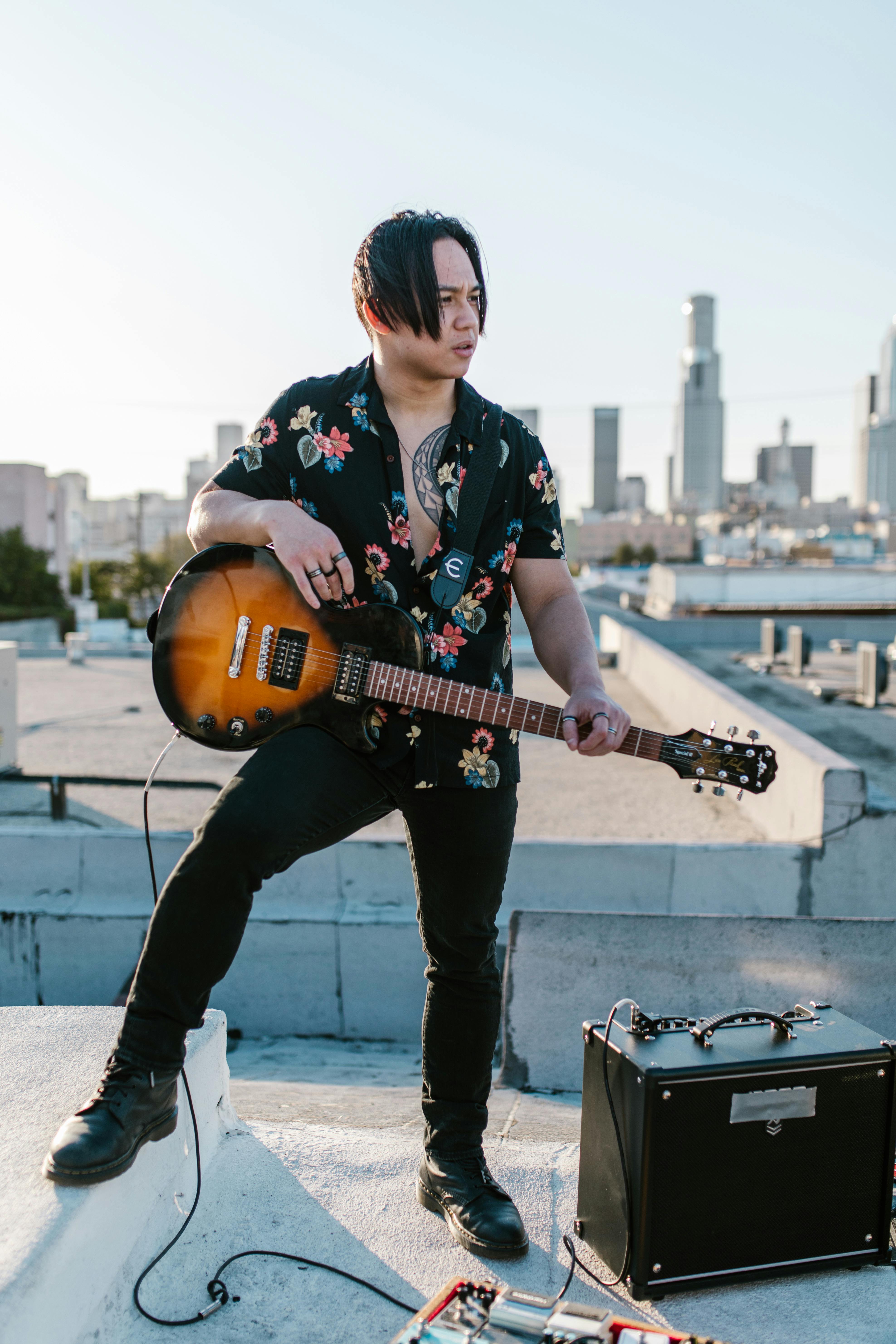 Musician playing electric guitar on rooftop with city skyline background.
