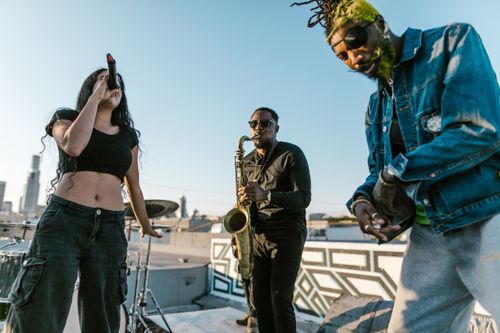 Free Energetic rooftop band playing at sunset, featuring saxophonist, singer, and guitarist. Stock Photo