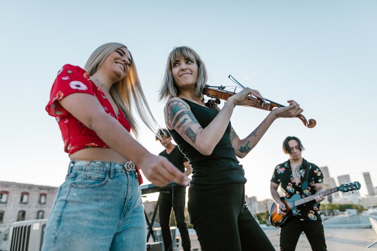 Woman In Black Shirt Playing The Violin Beside Woman In Red Top