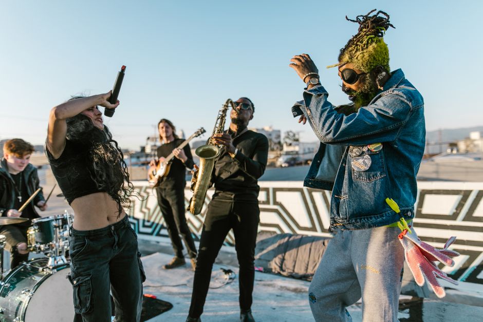 A dynamic music performance on a rooftop featuring a diverse band with musicians playing instruments and dancing.