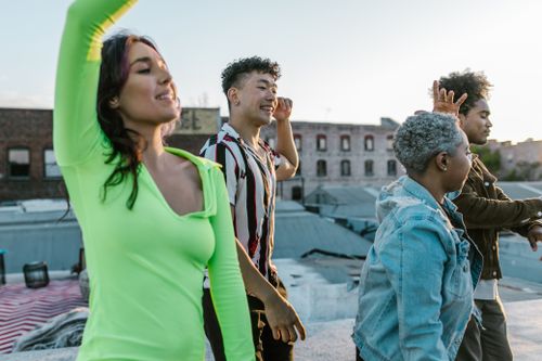 Free A lively group of diverse friends enjoying a dance on a city rooftop at sunset. Stock Photo