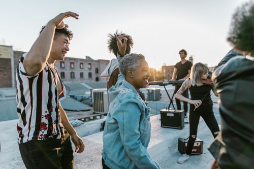 Free Group of musicians enjoying a lively rooftop dance party at sunset, creating a joyful atmosphere. Stock Photo