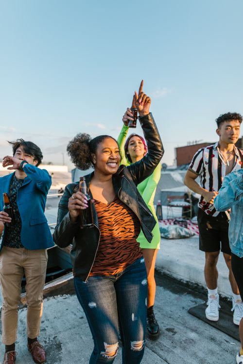 Free A group of diverse young adults enjoying a lively rooftop party under a clear blue sky. Stock Photo