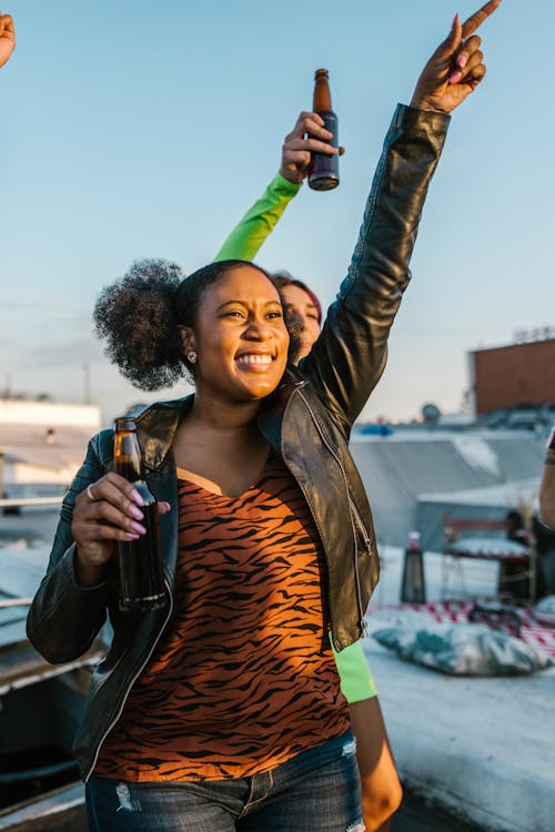 Smiling Woman in Brown Leather Jacket Holding Bottle of Beer