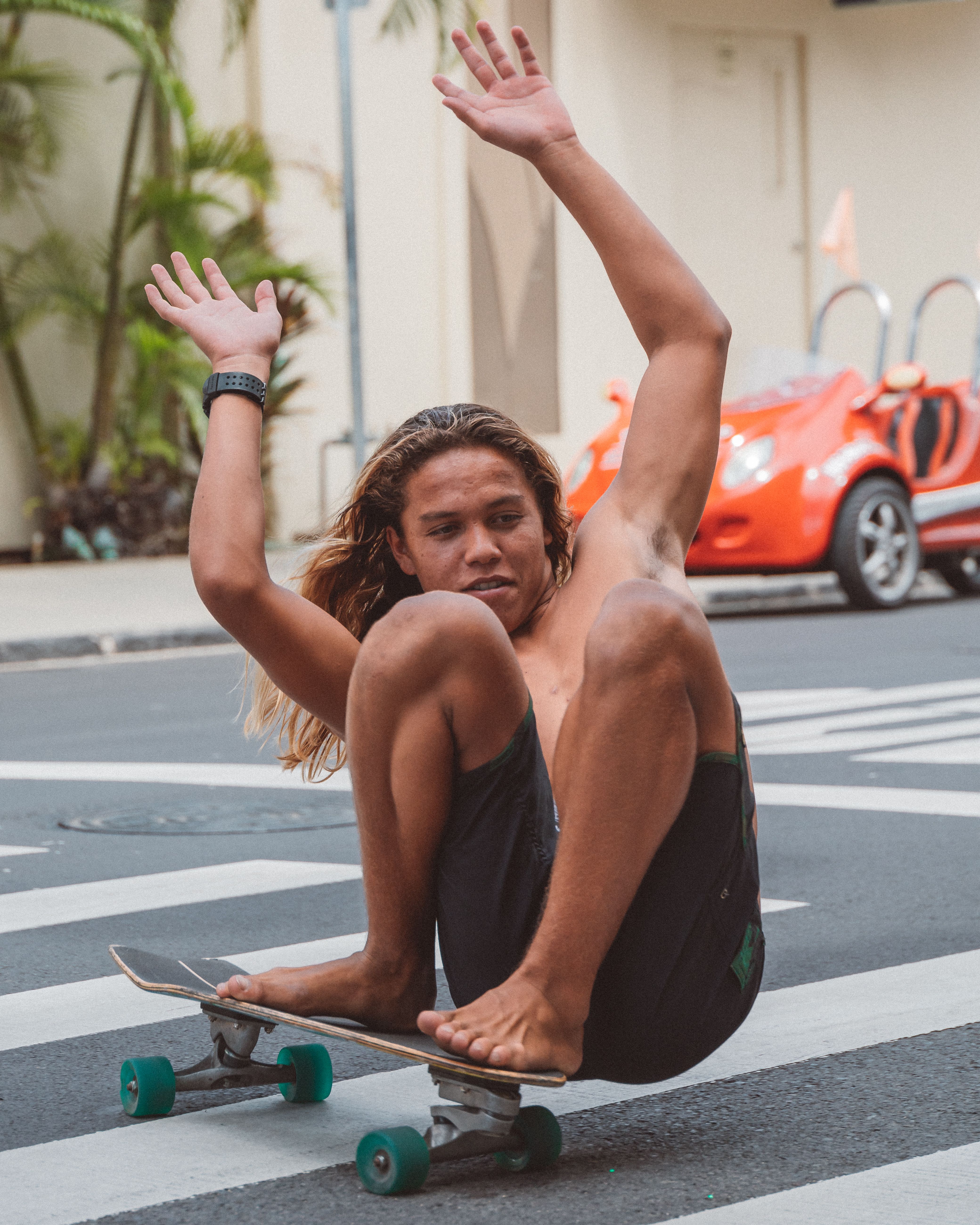 Young man skateboarding barefoot on street, performing tricks with hands raised in air.