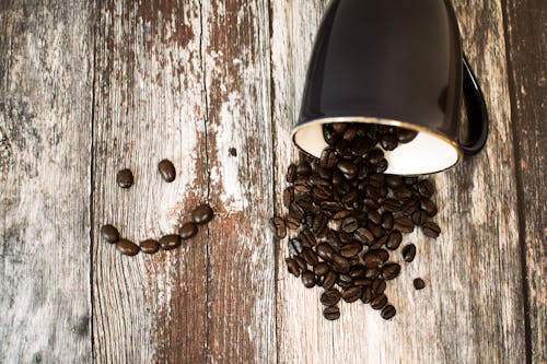免費 黑色的陶瓷杯，咖啡豆全部在褐色的木質表面上 圖庫相片