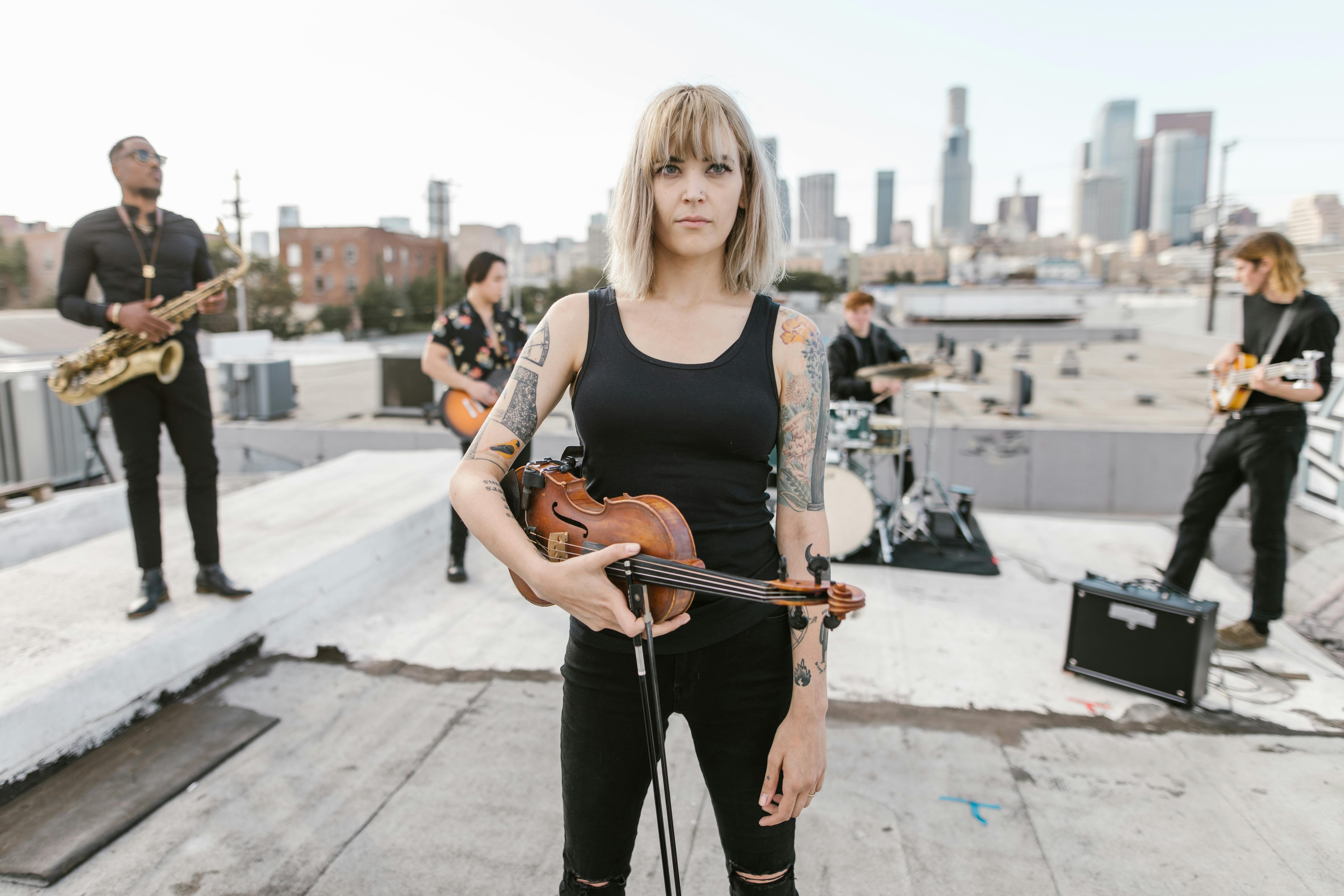 woman in black top holding violin while standing on the rood with music band behind