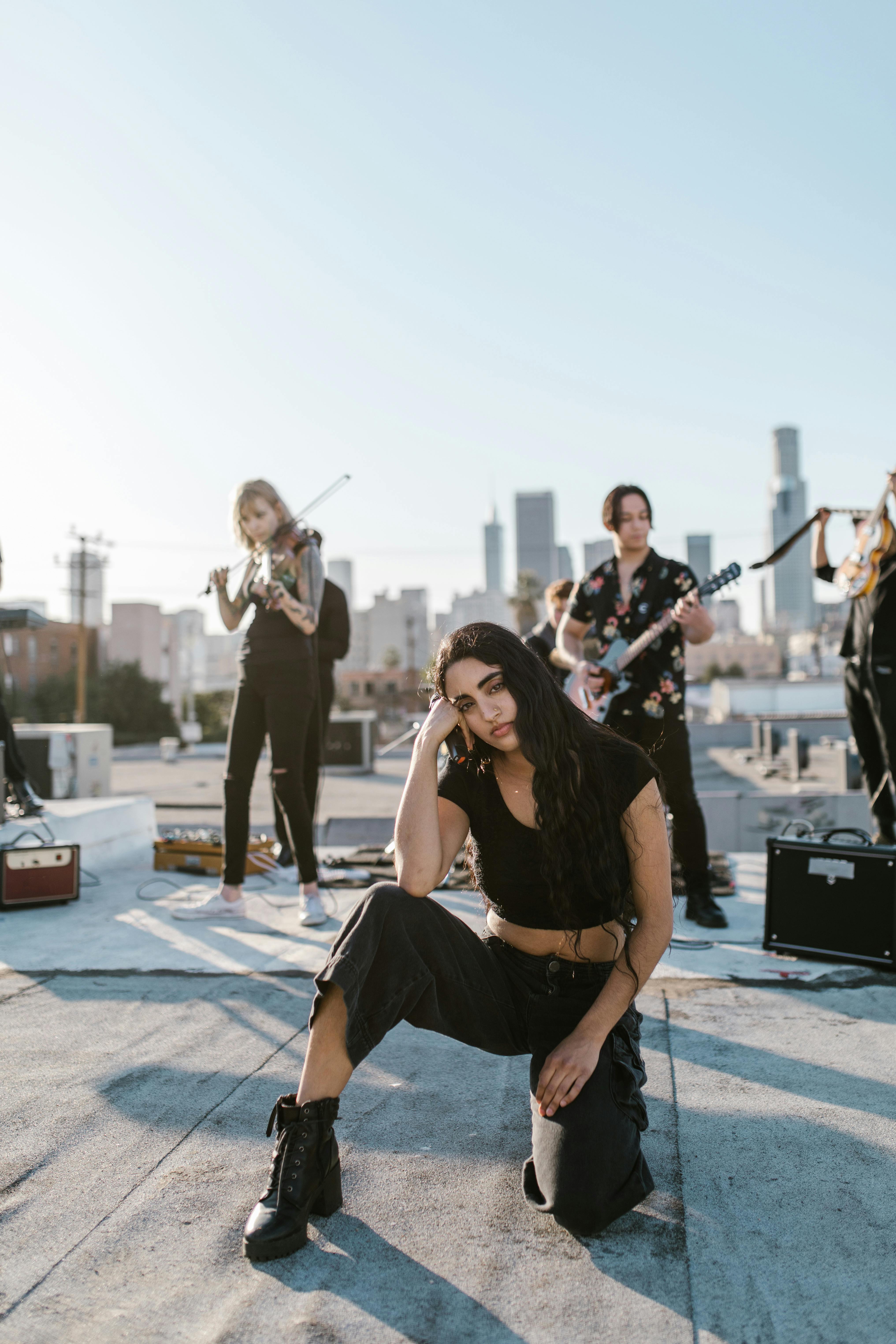 music band playing behind woman in black top and pants sitting on the rooftop