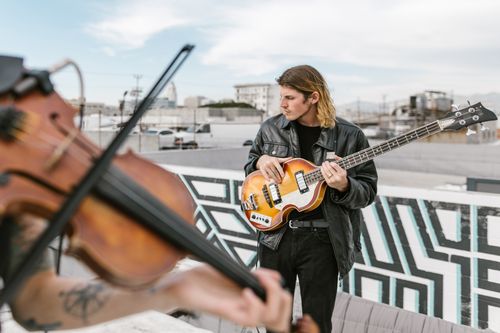 Free Musicians playing bass and violin on a rooftop, creating a dynamic urban performance scene. Stock Photo