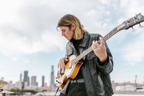 Free A young musician plays an electric bass guitar with a city skyline in the background. Stock Photo