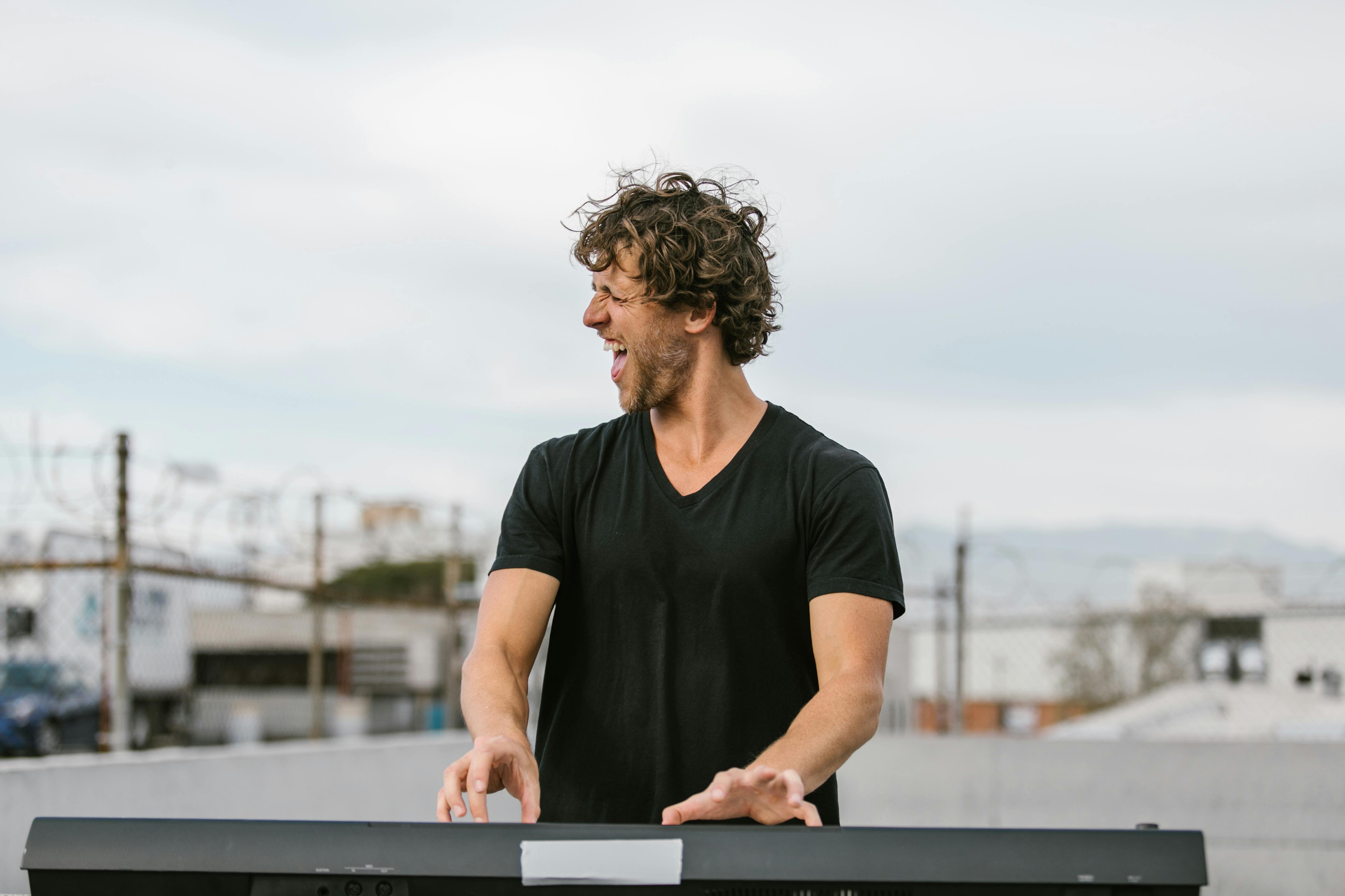 man in black t shirt playing on electronic keyboard and singing on the rooftop