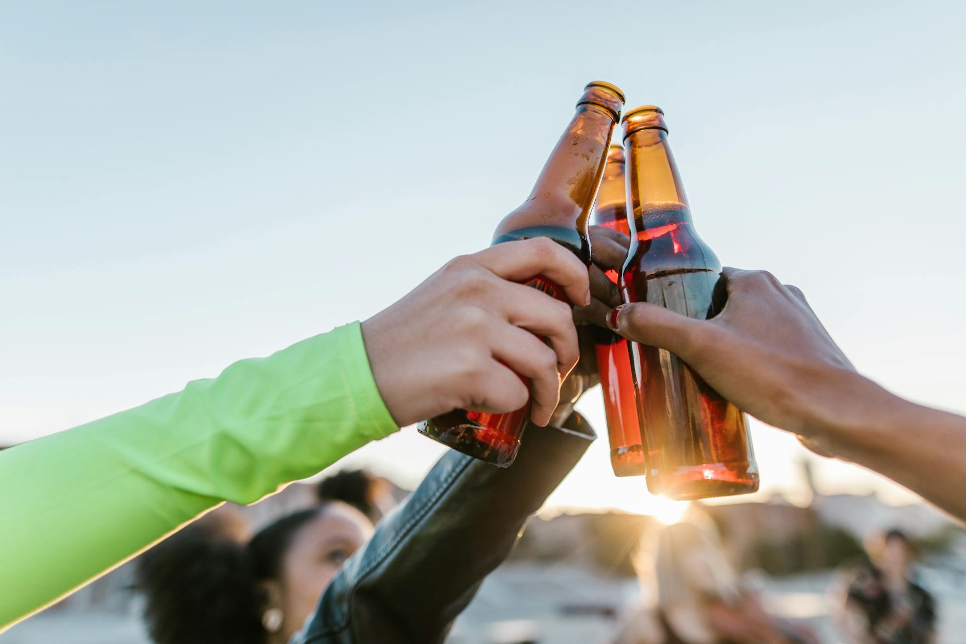 Group of friends toasting beer bottles at sunset, enjoying outdoor celebration.