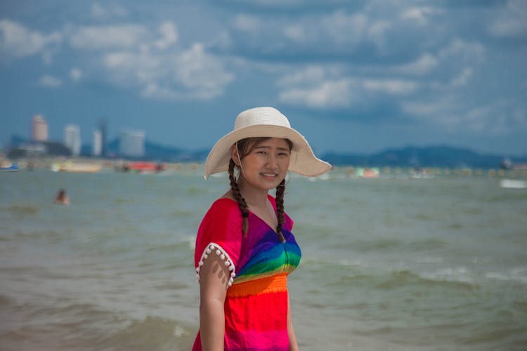 Girl With Braids In Colorful Top And Hat Standing On The Beach