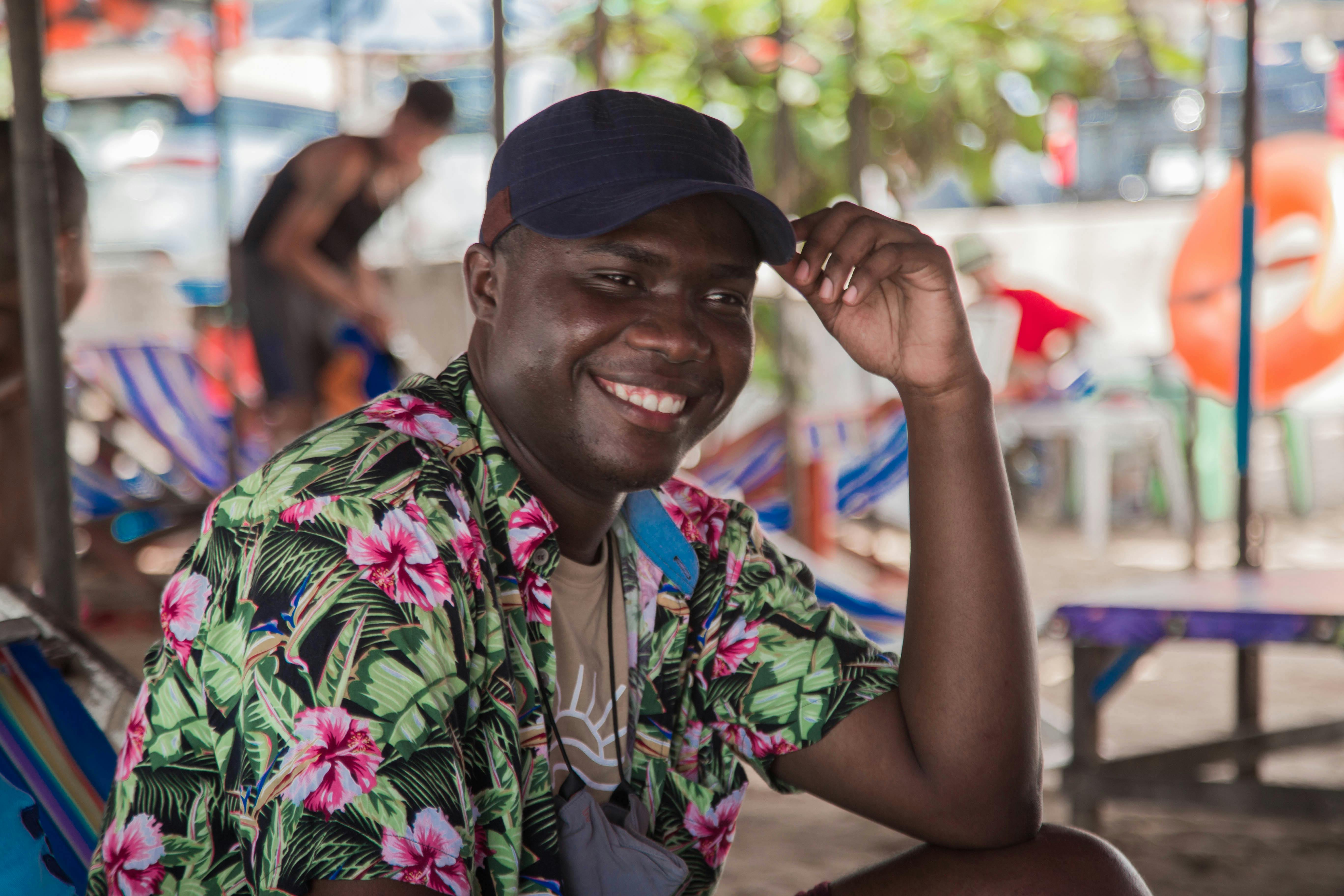 Free A cheerful man wearing a Hawaiian shirt relaxes at a vibrant beachside setting with lounge chairs. Stock Photo