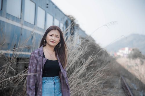 Free Portrait of a young woman in casual attire posing near a train in an outdoor setting. Stock Photo