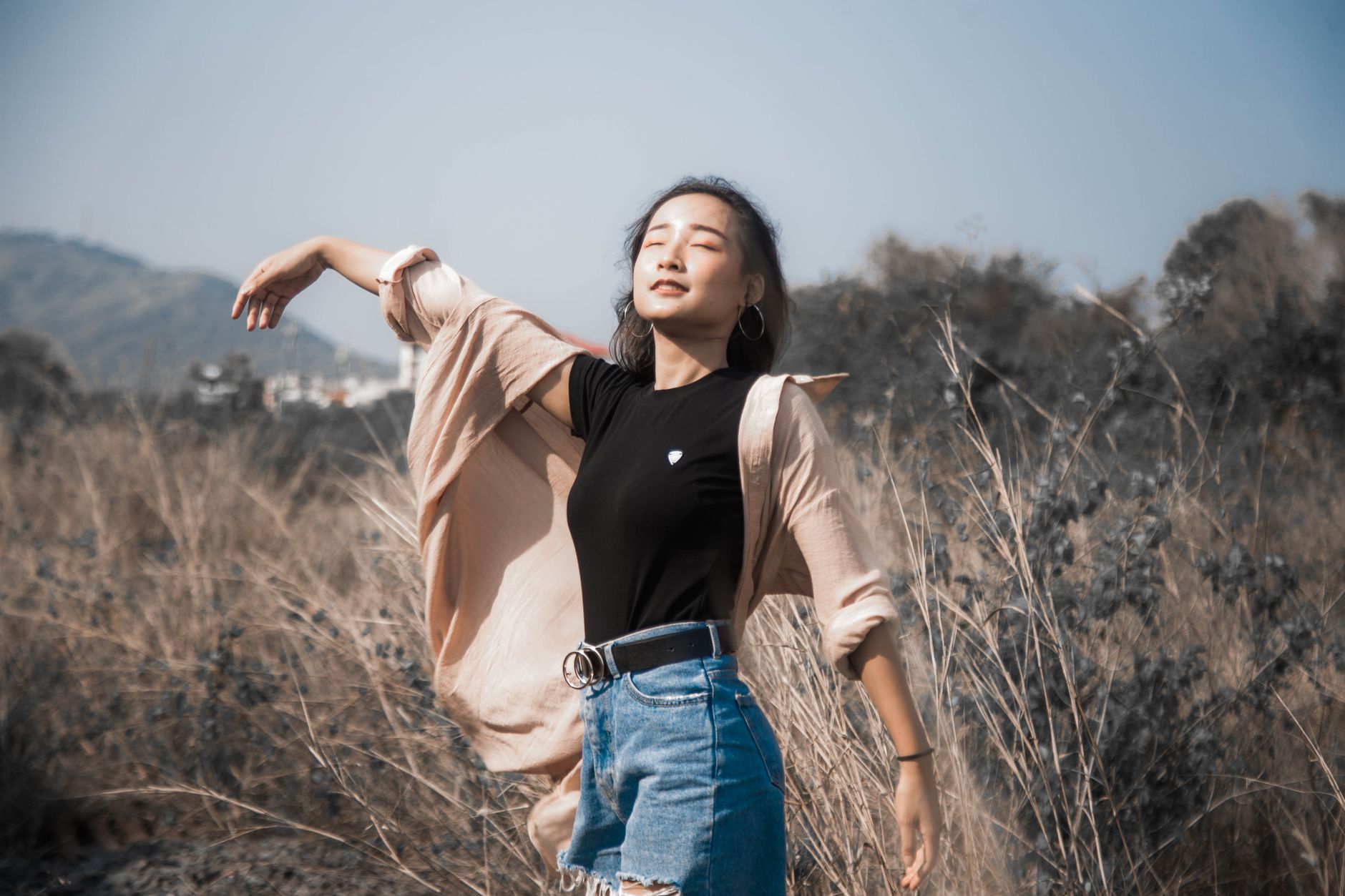 Asian woman relishing open air with eyes closed in a picturesque field, embodying freedom and serenity.