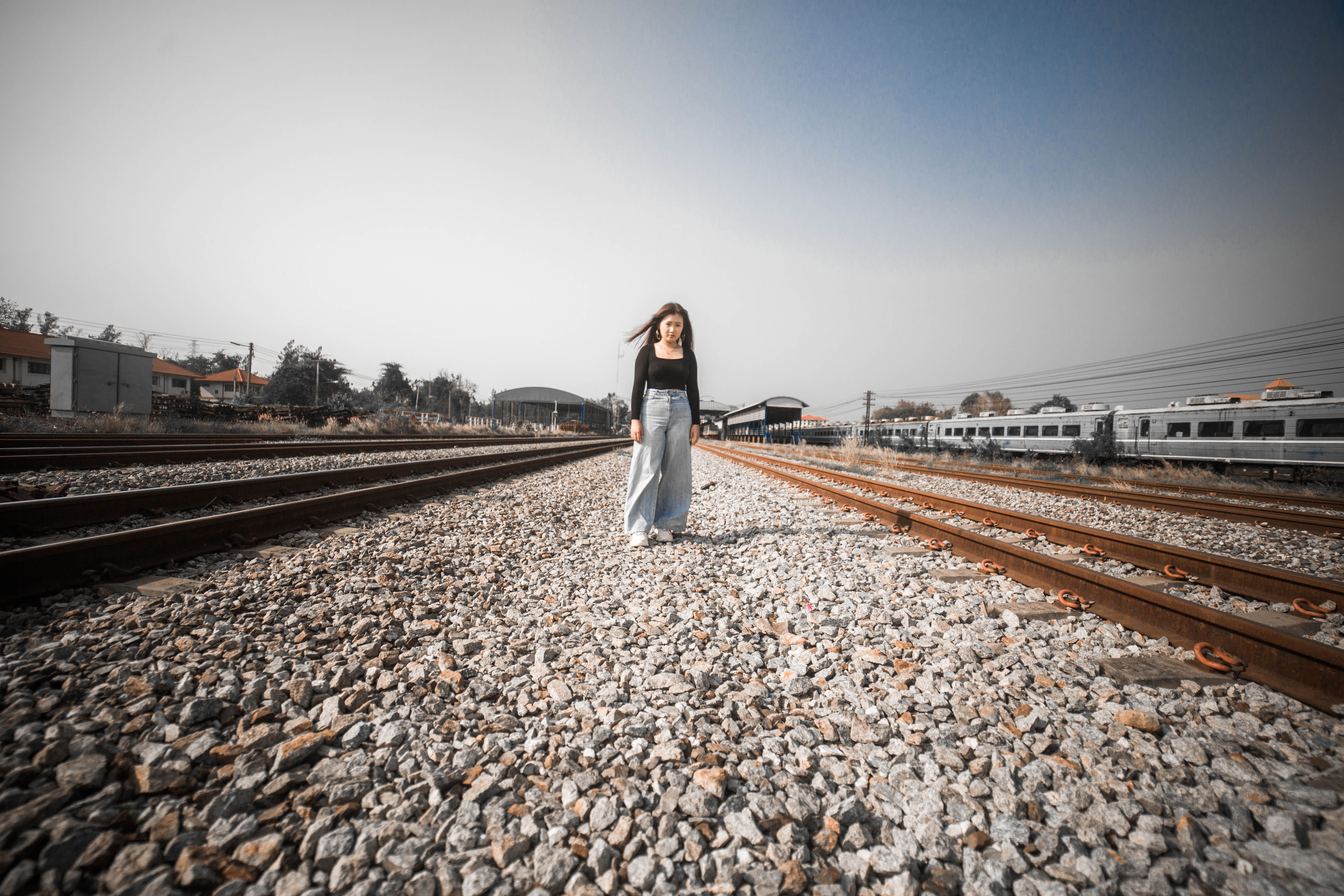 A woman walks confidently along railway tracks in an urban setting, showcasing travel and exploration.