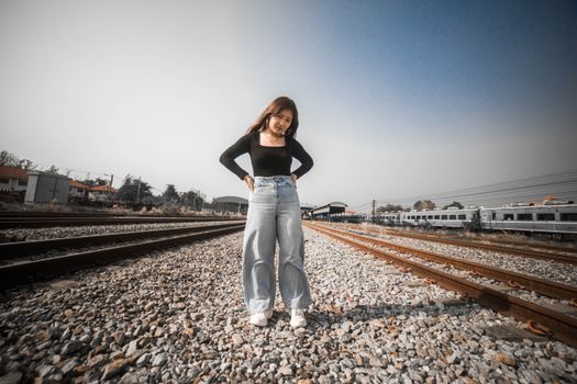 Stylish young woman posing confidently on railway tracks in a low angle shot outdoors.