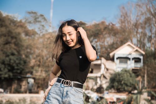 Free Smiling woman poses outdoors with hand in hair against a house backdrop. Stock Photo