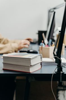 A warm workspace with books, computer, and person working, perfect for studying or remote work.
