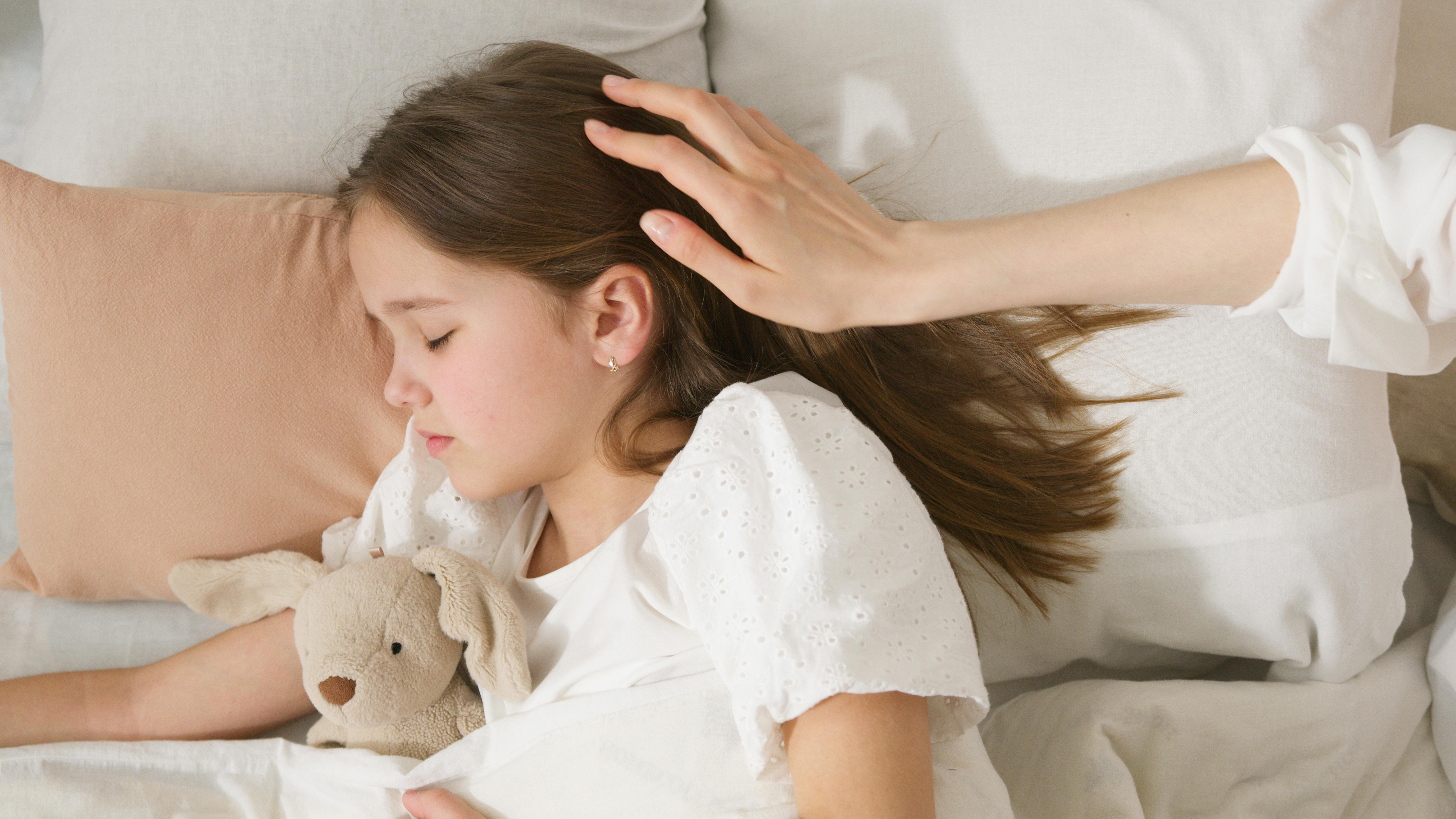 Young girl peacefully sleeping while being gently patted, holding a stuffed toy.